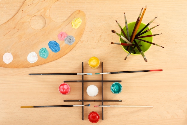 Palette mit bunten Farben und Pinseln in einer Tasse auf Holzschreibtisch Zeichenset