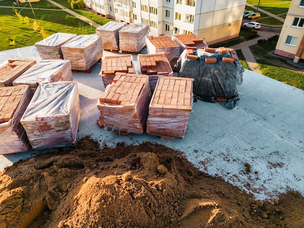 Paletten mit roten Keramikziegeln auf dem Dach eines im Bau befindlichen Gebäudes Vorbereitende Arbeiten zum Verlegen von Ziegeln Draufsicht auf die Baustelle