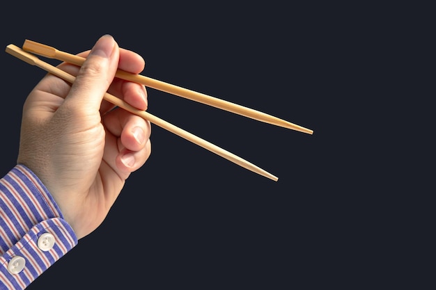 Palillos de bambú en una mano masculina sobre un fondo oscuro para la comida