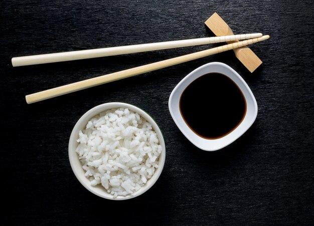 Los palillos japoneses del sushi sobre la salsa de soja ruedan, arroz en fondo negro