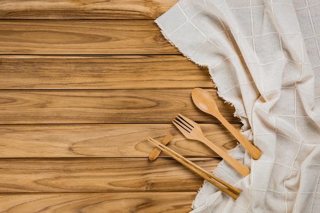 Los palillos de madera descansan sobre un paño blanco. Hay cuchara y tenedor sobre fondo de madera.