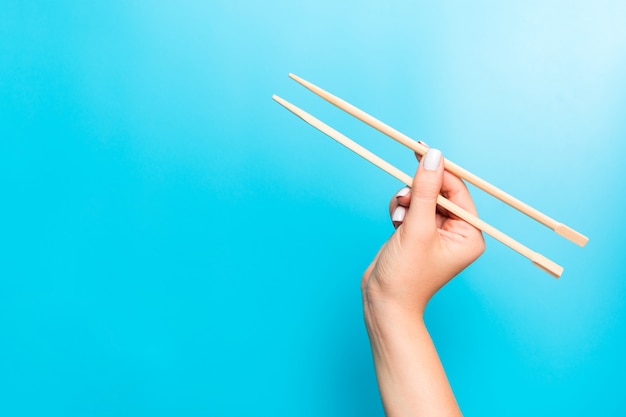 Palillos de madera sujetos con manos femeninas en azul. Listo para comer s con espacio vacío