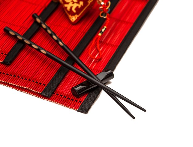 Palillos negros sobre estera de bambú rojo. Mesa de estilo asiático con amuleto de la suerte del año nuevo chino