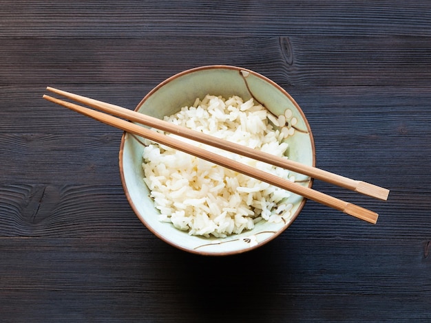 Palillos sobre arroz hervido en taza sobre mesa oscura