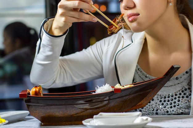 Foto palillos sosteniendo un camarón. chica joven con palillos. sabor inolvidable de la cocina japonesa. el almuerzo más delicioso.