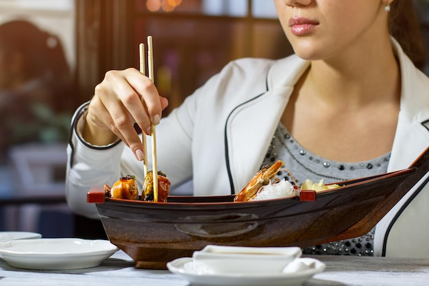 Los palillos sostienen el rollo de sushi. Chica joven con palillos. Gourmet disfruta de una sabrosa comida. Cena en restaurante japonés.