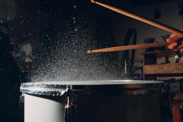 Palillos de tambor que golpean el ritmo en la superficie del tambor con gotas de agua de salpicadura