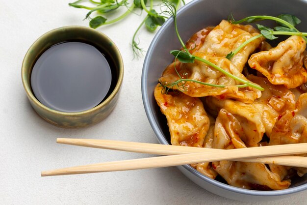 Palillos en un tazón de albóndigas gyoza Salsa de soja en un tazón Brotes de guisantes verdes sobre la mesa Plano Fondo blanco