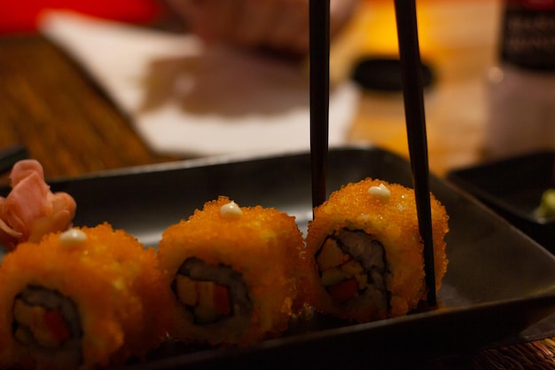 Palillos tomando rollo de sushi con tobiko naranja. Comida tradicional japonesa, conceptos de bajo perfil