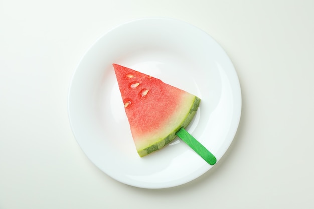 Palito de hielo con una rodaja de sandía en un plato sobre fondo blanco.