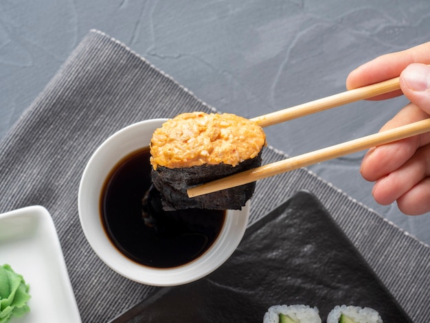 Los palitos de bambú sostienen un gunkan afilado. Al fondo hay un cuenco de salsa de soja. De cerca. cocina tradicional japonesa