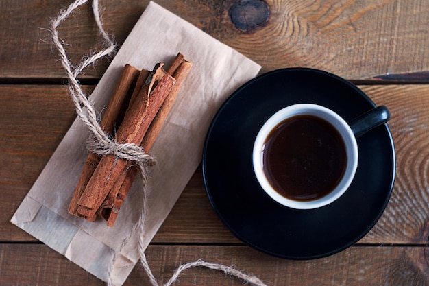 Palitos de canela atados con una cuerda yacen sobre una mesa de madera. Hay una taza de café cerca.