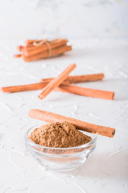 Foto palitos de canela, atados con una soga, y canela molida en un tazón yacen sobre la mesa.