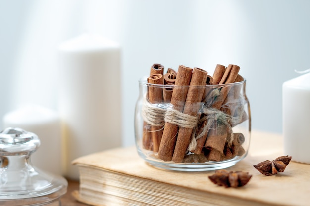 Palitos de canela en frasco de vidrio, estrella de anís, velas, libro vintage en la vieja mesa de madera rústica rústica. Acogedor bodegón.