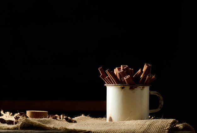 Palitos de canela en una vieja taza de metal sobre una mesa negra. especia aromática