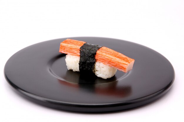 Palitos de cangrejo de sushi con una placa negra sobre un fondo blanco.