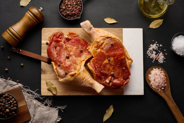 Palitos de frango crus temperados em uma tábua de madeira acompanhados de sal e pimenta