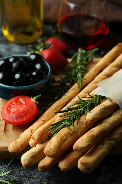 Palitos de grissini, salgadinhos e vinho na superfície preta esfumada