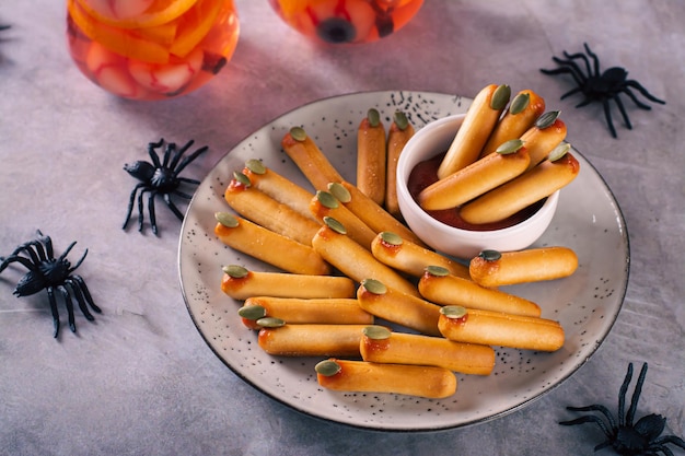 Palitos de pão saborosos de Halloween com unhas de sementes de abóbora em ketchup em um prato