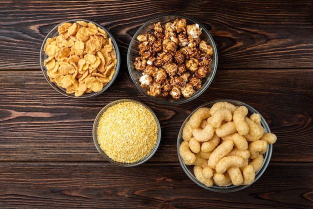 Palitos de maíz, copos de maíz y palomitas de maíz sobre fondo de madera oscura.