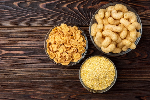 Palitos de maíz, copos de maíz y palomitas de maíz sobre fondo de madera oscura.