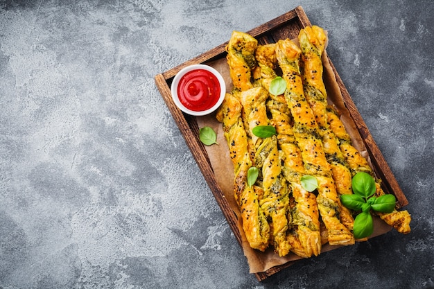 Palitos de pan casero con queso, salsa pesto y semillas de sésamo negro sobre superficie vintage de piedra gris