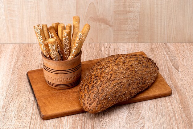 Palitos de pan crujiente con semillas de sésamo y pan de salvado sobre una tabla de madera.