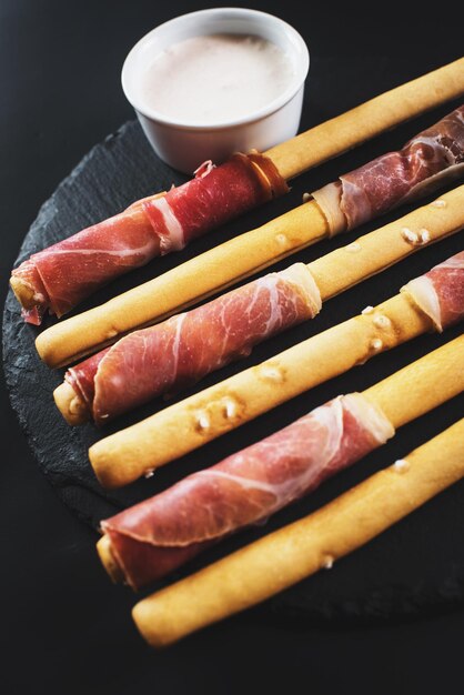 Palitos de pan envueltos en jamón sobre fondo negro