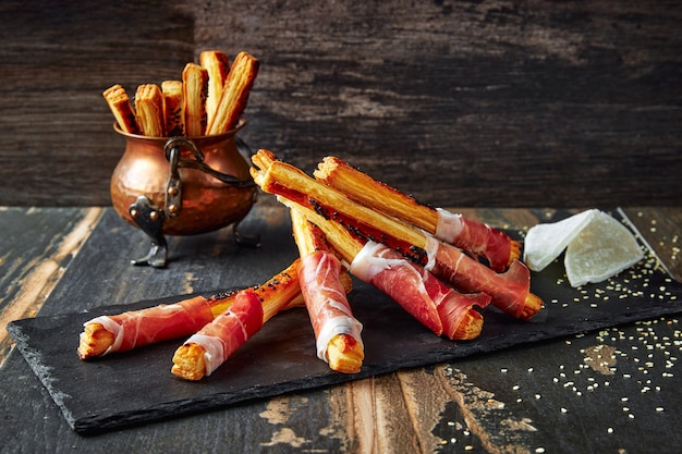 Palitos de pan Grissini enrollados con jamón prosciutto sobre una tabla