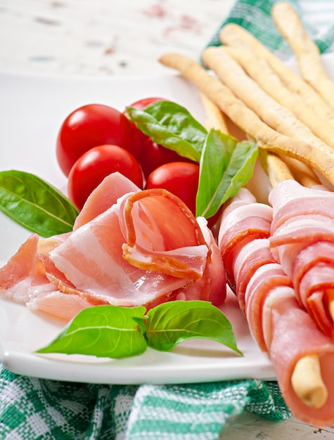 Foto palitos de pan grissini con jamón, tomate y albahaca