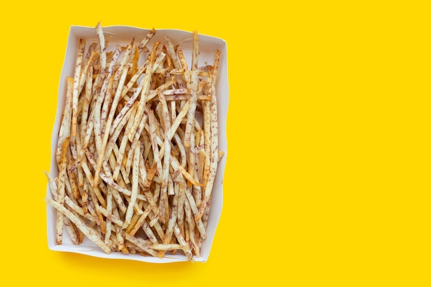 Palitos de taro frito en caja de papel sobre fondo amarillo.