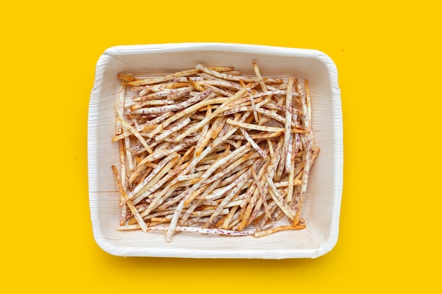 Palitos de taro frito en placa sobre fondo amarillo.