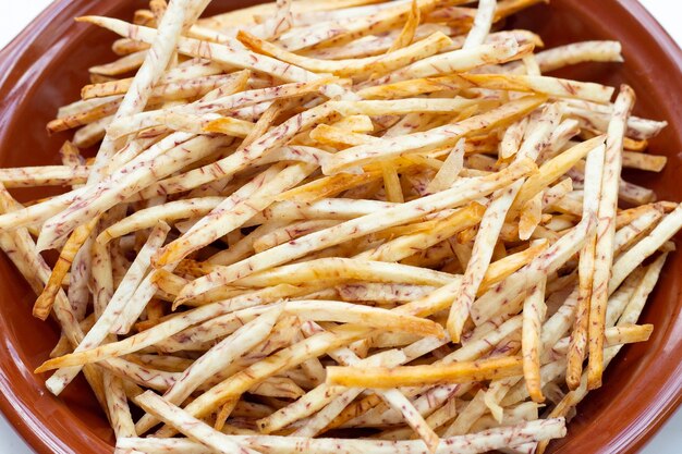 Foto palitos de taro fritos en un tazón sobre fondo blanco.