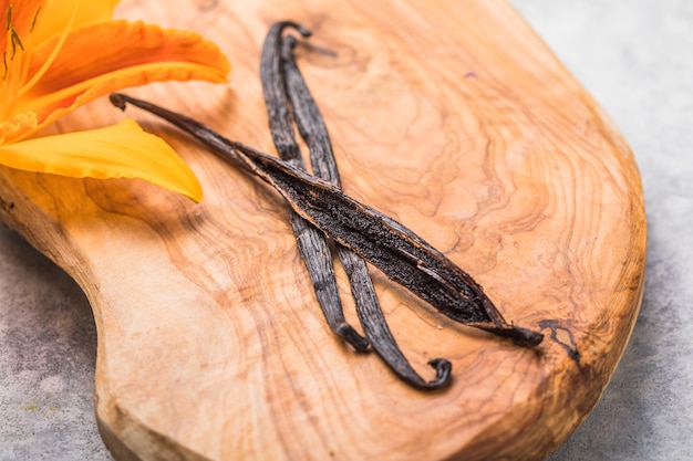 Palitos de vainilla secos y flor de orquídea de vainilla en una mesa de madera Closeup