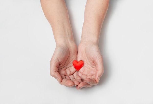 Las palmas femeninas sostienen un pequeño corazón rojo Símbolo de protección del amor