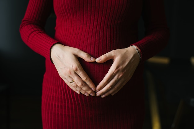 Palmas en forma de corazón en el vientre de una mujer embarazada con un vestido burdeos