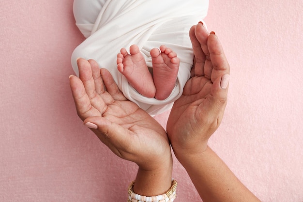 Las palmas de las manos del padre la madre están sosteniendo el pie del bebé recién nacido en una manta blanca fondo rosado los pies del recién nacido en las palmas de la mano de los padres foto de los dedos de los pies y los talones de los niños