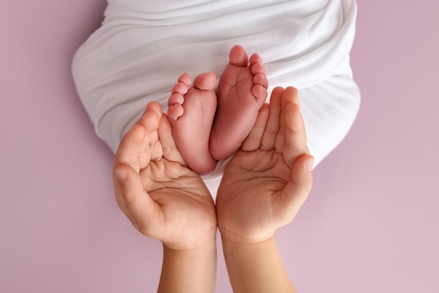 Las palmas de las manos del padre la madre están sosteniendo el pie del bebé recién nacido en una manta blanca los pies del recién nacido en las palmas de los padres Estudio foto macro de los dedos de los pies y los talones de un niño