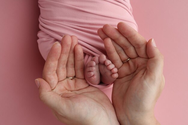 Las palmas de las manos del padre la madre están sosteniendo el pie del bebé recién nacido en una manta rosada los pies del recién nacido en las palmas de los padres Estudio foto macro de los dedos de los pies y los talones de un niño