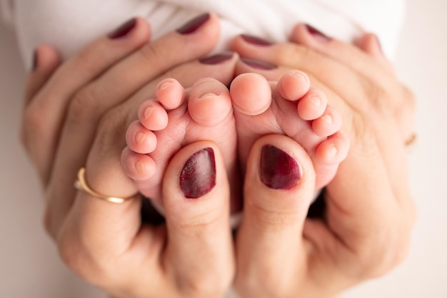 Las palmas de los padres Un padre y una madre sostienen los pies de un recién nacido en una sábana blanca sobre un fondo blanco Los pies de un recién nacido en manos de los padres Foto de talones y dedos de los pies