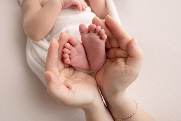 Las palmas de los padres Un padre y una madre sostienen los pies de un recién nacido en una sábana blanca sobre un fondo blanco Los pies de un recién nacido en manos de los padres Foto de talones y dedos de los pies