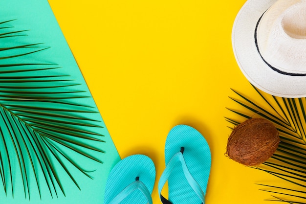 Palmblätter-Kokos-Flip-Flops und Sommerhut auf gelber und türkisfarbener Textur Sommer- und Urlaubskonzept Draufsicht flach mit Kopierraum