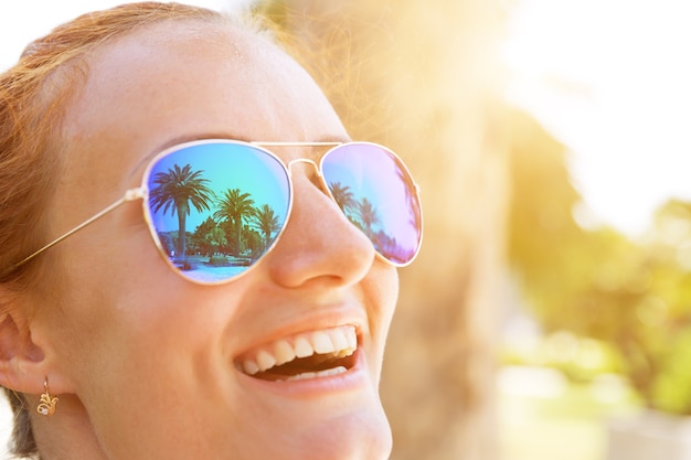 Palmen spiegeln sich in der Sonnenbrille des glücklichen Mädchens wieder