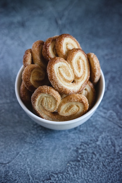 Palmier Puff Pastelaria. Deliciosos biscoitos palmier francês com açúcar em uma tigela branca na superfície escura