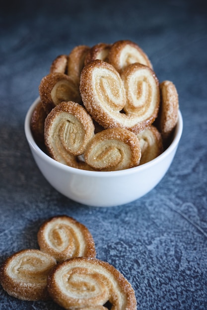 Palmier Puff Pastelaria. Deliciosos biscoitos palmier francês com açúcar em uma tigela branca na superfície escura