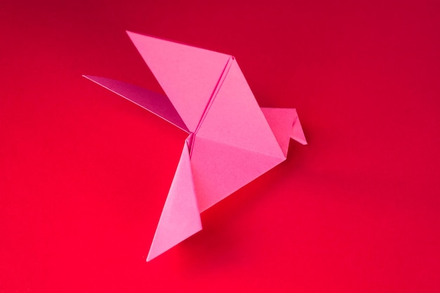 Paloma de papel rosa origami aislado sobre un fondo rojo.