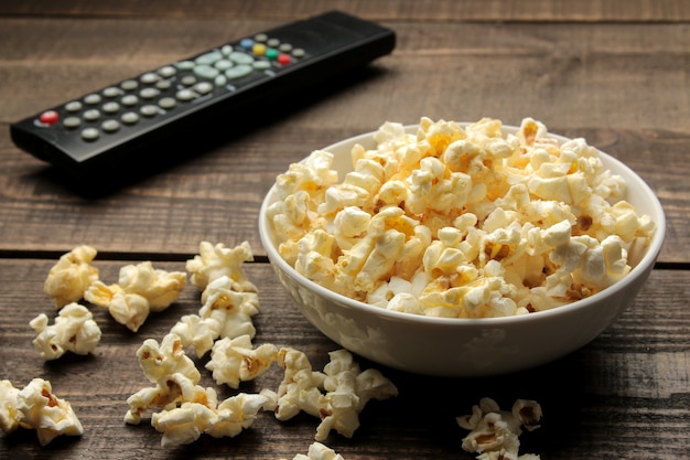 Palomitas de maíz y control remoto de TV en una mesa de madera marrón, concepto de ver películas en casa.