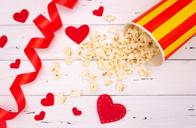 Palomitas de maíz, corazones rojos y cinta sobre un fondo de madera blanca. dia de san valentin, cine.