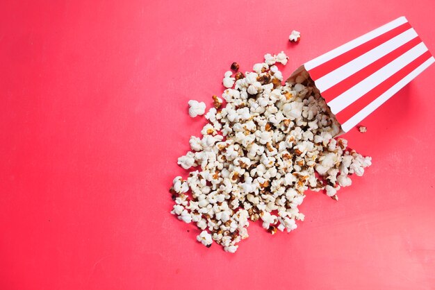 Palomitas de maíz derramándose de un recipiente sobre fondo rojo.