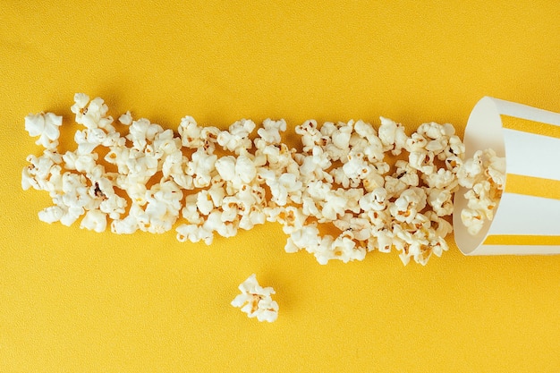 Palomitas de maíz esparcidas de un vaso de papel rayado. el concepto de cine en casa y películas en el cine.